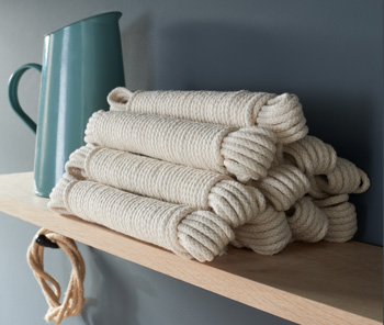 Bundles of our cotton pulley ropes and sash cord sat in a pile on a shelf. There is a green jug in the back ground and a bundle of jute cord hanging from a hook.